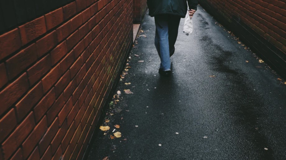 brick wall and person with jeans walking on asphalt walkway